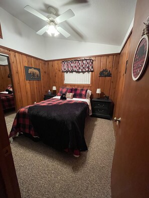 Un dormitorio con cama, mesita de noche, cómoda, ventilador de techo y ventana con cortinas.