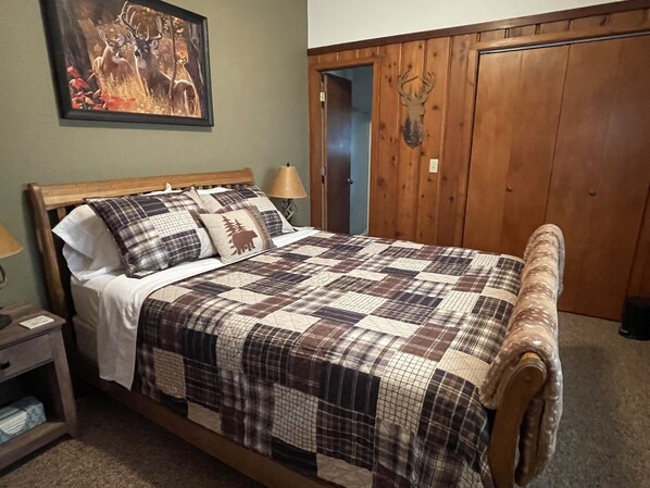 Un lit avec une couvre-lit à carreaux, une tête de lit en bois et une table de chevet avec une lampe.