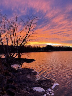 Vista del lago con árboles y un atardecer.