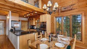 A spacious wooden cabin with a dining area, kitchen, and a large window overlooking a forest. - LOG CABIN w/Mtn View, Hot Tub, & Fireplace! (Divide)
