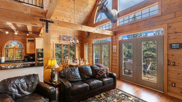 A wooden cabin interior with a leather sofa, dining table, and a mounted deer head. - LOG CABIN w/Mtn View, Hot Tub, & Fireplace! (Divide)