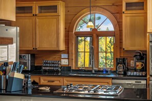 A kitchen with wooden cabinets, a stainless steel refrigerator, a coffee maker, and a window with a view of trees.