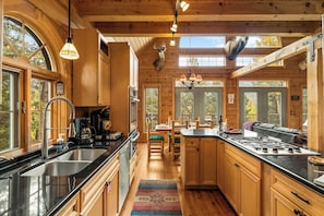 A spacious kitchen with wooden cabinets, a large island, and a dining area with a view of the outdoors. - LOG CABIN w/Mtn View, Hot Tub, & Fireplace! (Divide)