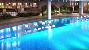 A modern hotel with a swimming pool, sun loungers, and a well-lit outdoor area.