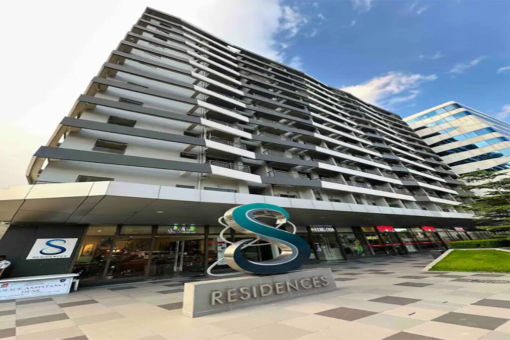A high-rise building with a modern design, featuring multiple balconies and a prominent logo at the entrance.