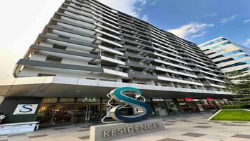 A high-rise building with a modern design, featuring multiple balconies and a prominent logo at the entrance.