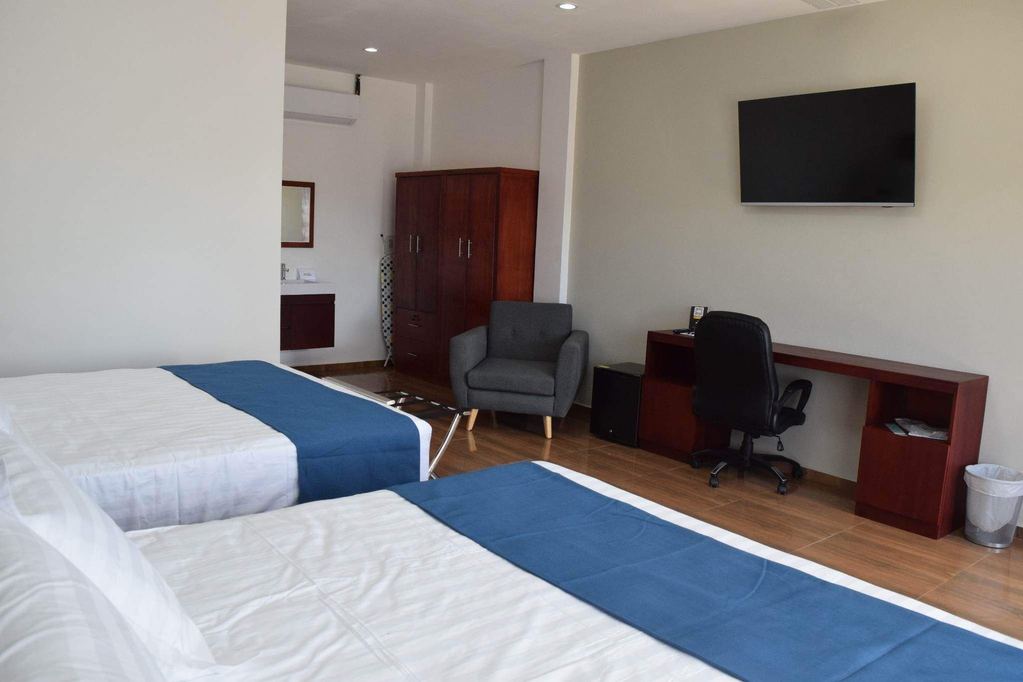 A hotel room with two beds, a desk, a chair, a television, and a wardrobe.