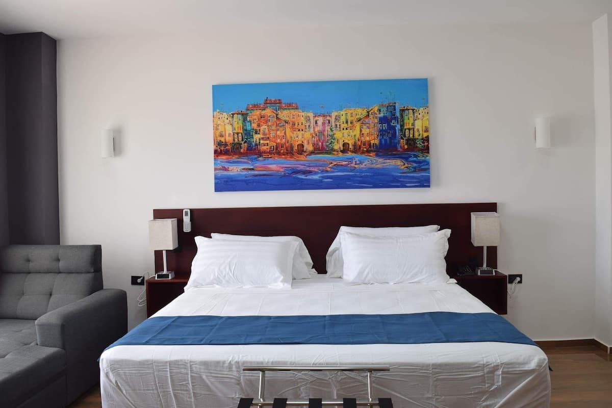 Ein Hotelzimmer mit einem Bett, zwei Nachttischlampen, einem Sessel und einem Bild an der Wand.