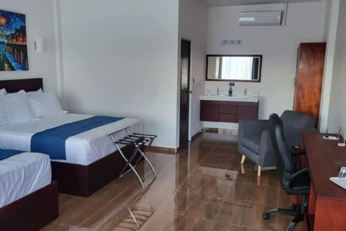 Ein Hotelzimmer mit Bett, Schreibtisch, Stuhl, Spiegel und einer kleinen Küchenzeile.