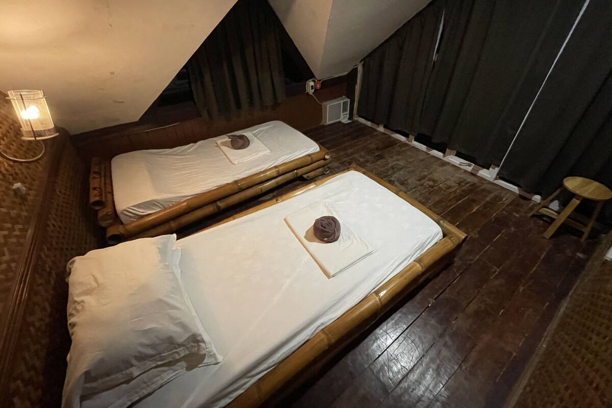 Two single beds with wooden frames and white linens in a room with dark wooden flooring and a sloped ceiling.