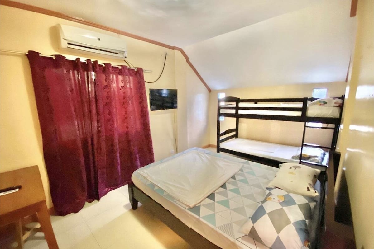 A small, single-room accommodation with bunk beds, a desk, and an air conditioning unit.