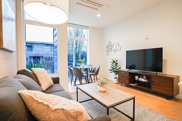 This main living space on the second floor features an open floor plan that includes a fully equipped kitchen with gorgeous quartz countertops, high-end stainless-steel appliances, a breakfast bar, dining table, and living room
