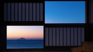 Habitación con vista al océano al atardecer, una bañera de madera y una ventana con persianas verticales.