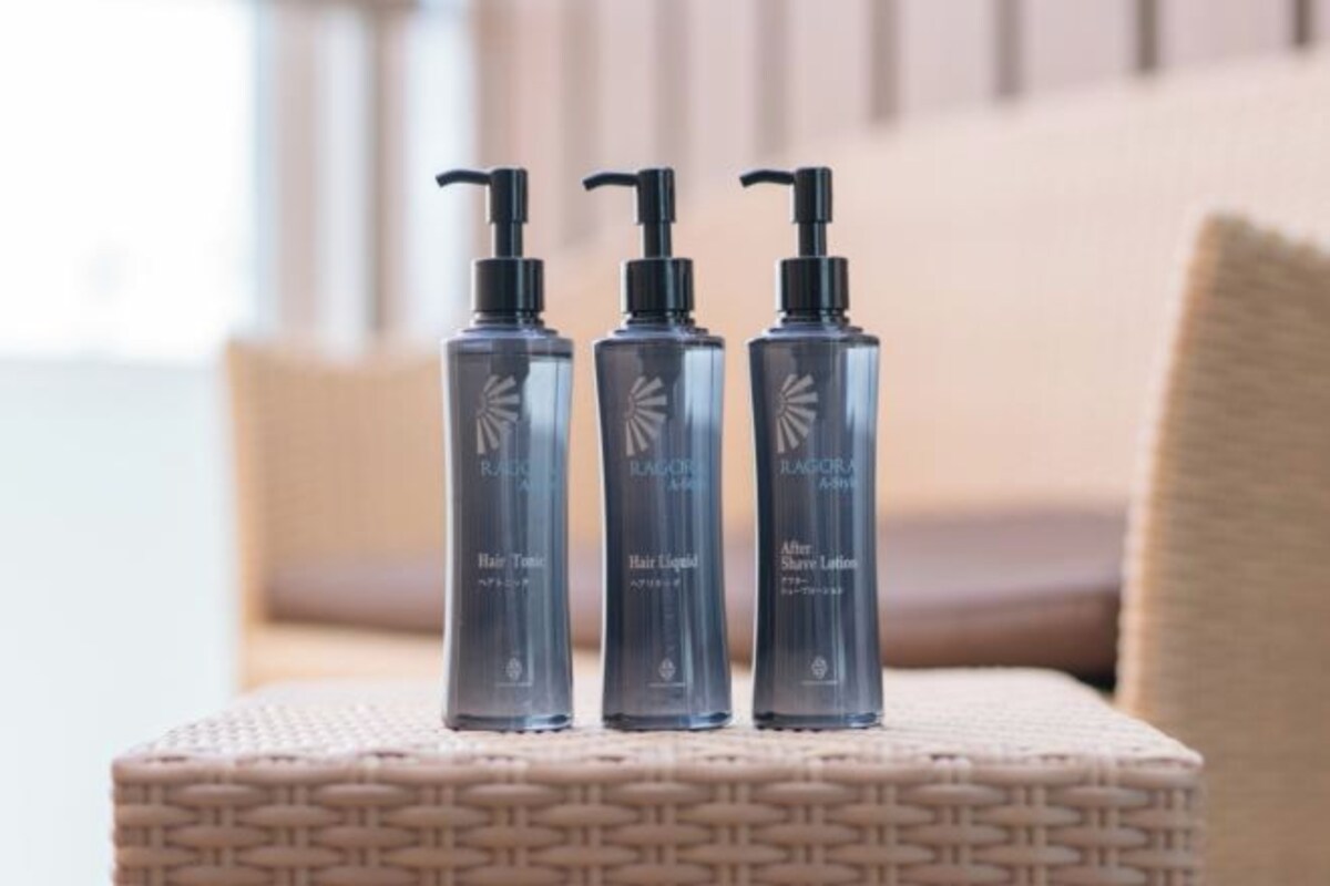 Tres botellas de productos para el cuidado del cabello sobre un taburete tejido.