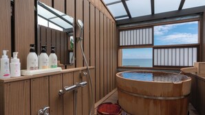 Un área de spa de madera con una bañera de hidromasaje, armarios de madera y vistas al mar.