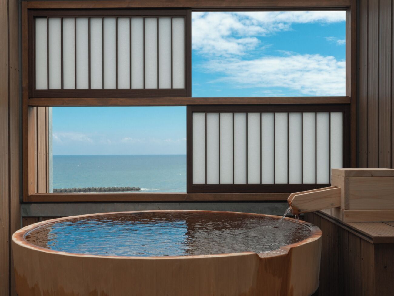 Eine Holzwanne mit Blick auf das Meer durch ein Fenster mit vertikalen Rollläden.