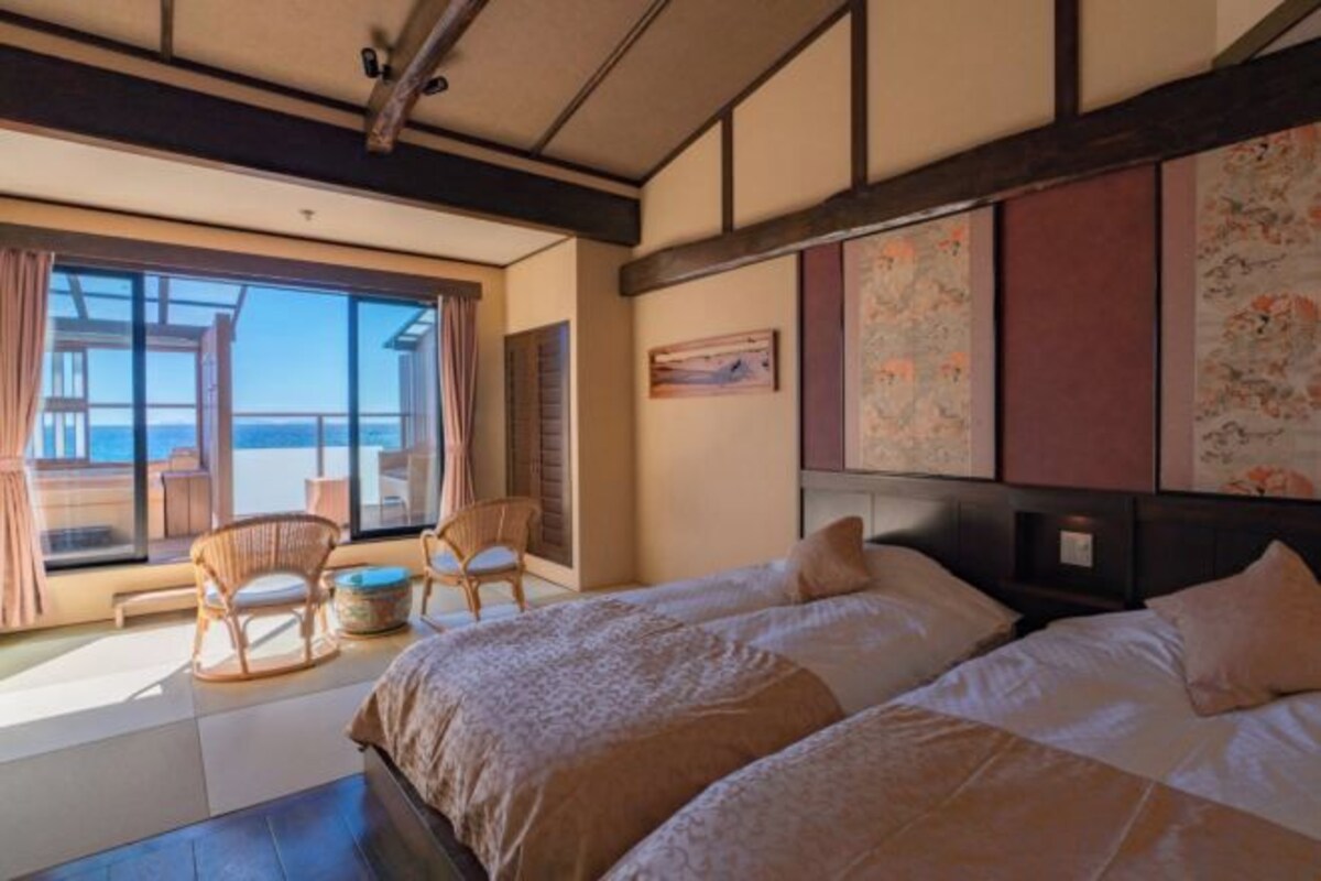 Habitación de hotel con un ventanal que ofrece vistas al mar, una cama con cabecera y una zona de estar con sillas.