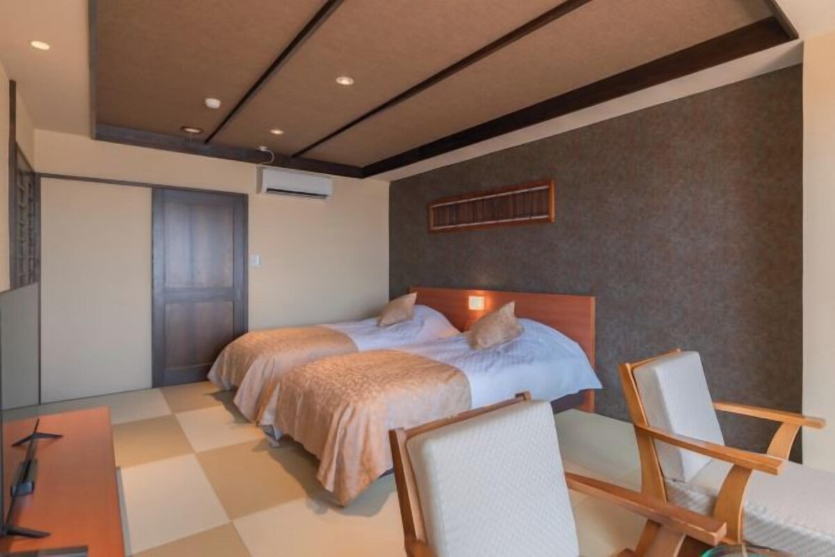 A hotel room with two beds, a desk, and a chair.