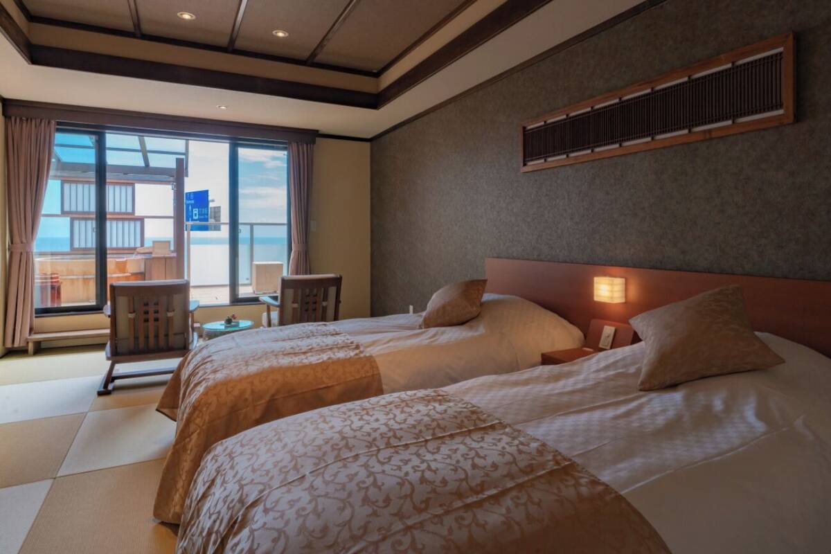A hotel room with two beds, a balcony with a view, a small table, and a chair.
