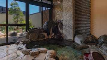 Un bain à remous en pierre, au design rustique, entouré de rochers et agrémenté d’une petite cascade.