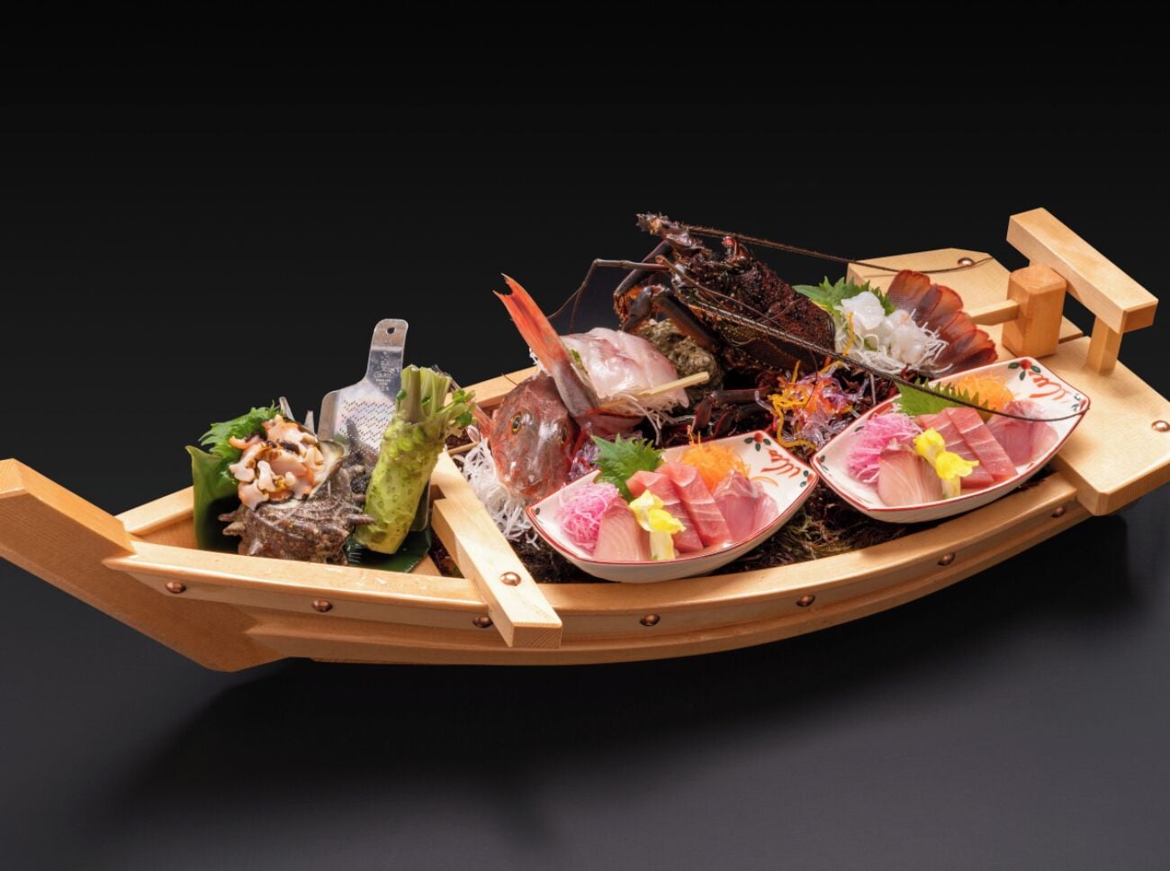 Un bote de madera lleno de diversos platos de mariscos, como sashimi y langosta, sobre un fondo oscuro.