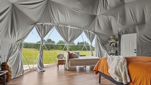 A tented room with a bed, bedside table, and a view of a grassy field. - Spa Weekend Near WinStar Spa or Golf Included (Thackerville)