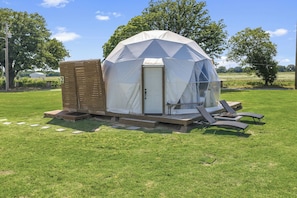 A geodesic dome structure with a door and steps leading up to it, surrounded by a grassy field.