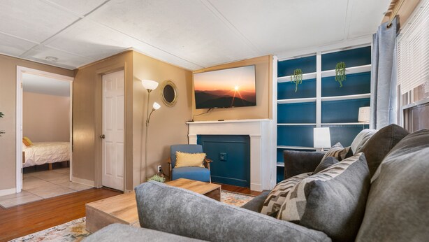 A living room with a sofa, a blue armchair, a fireplace, and a TV mounted above it. - King Bed Private Parking  Fast Internet (Poughkeepsie)