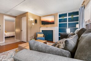 A living room with a sofa, a blue armchair, a fireplace, and a TV mounted above it.