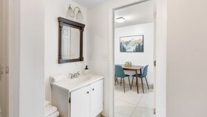 A bathroom with a white sink, a mirror, and a towel rack. There is a door leading to a dining area with a table and chairs. - King Bed Private Parking  Fast Internet (Poughkeepsie)