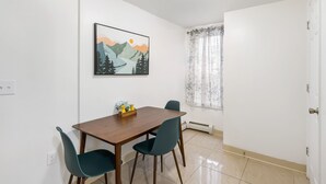A dining area with a wooden table and two chairs, a painting on the wall, and a window with curtains. - King Bed Private Parking  Fast Internet (Poughkeepsie)