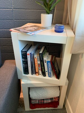 A cozy reading nook features a two-tiered bookshelf with a potted plant and books.