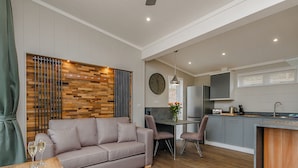 Un salon moderne comprenant un canapé, une table à manger et des chaises, une cuisine avec des placards et des appareils électroménagers, et un mur décoratif en bois.