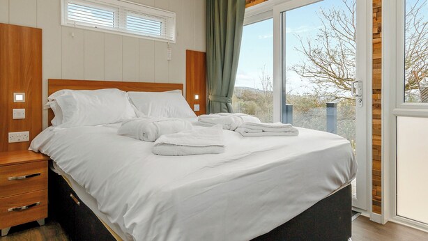 Une chambre à coucher avec un lit, des tables de chevet, une fenêtre avec des rideaux et une vue sur l’extérieur.