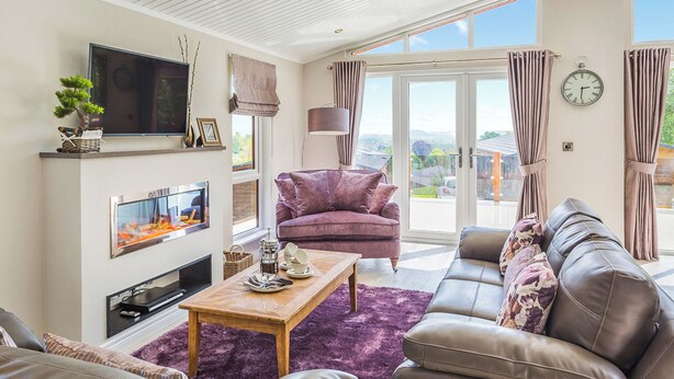 Ein modernes Wohnzimmer mit Flachbildfernseher, Kamin, Sofa, Couchtisch und Blick durch große Glasschwingtüren.