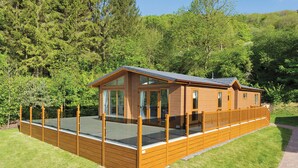 Eine Holzhütte mit einer Terrasse, großen Fenstern und Blick auf den umliegenden Wald.