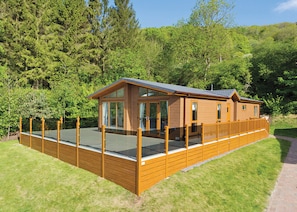 A wooden cabin with a deck, large windows, and a view of the surrounding forest.