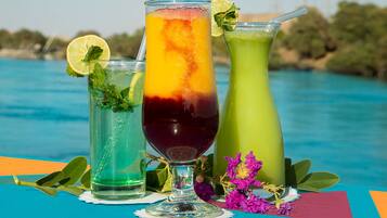 Three colorful drinks with garnishes, placed on a table by a body of water.