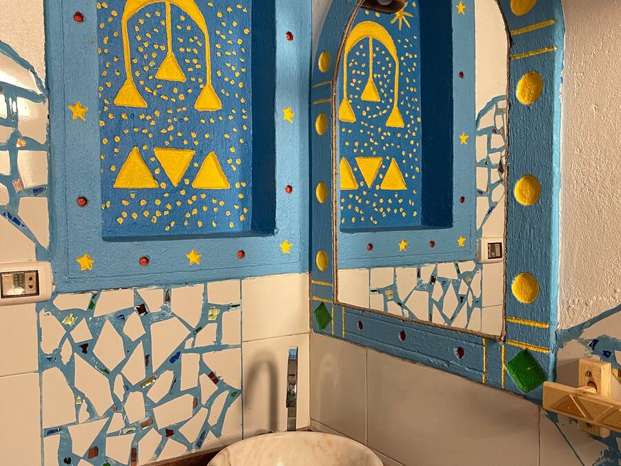 A bathroom with a mosaic tile wall, a large sink, and decorative elements like bells and stars.