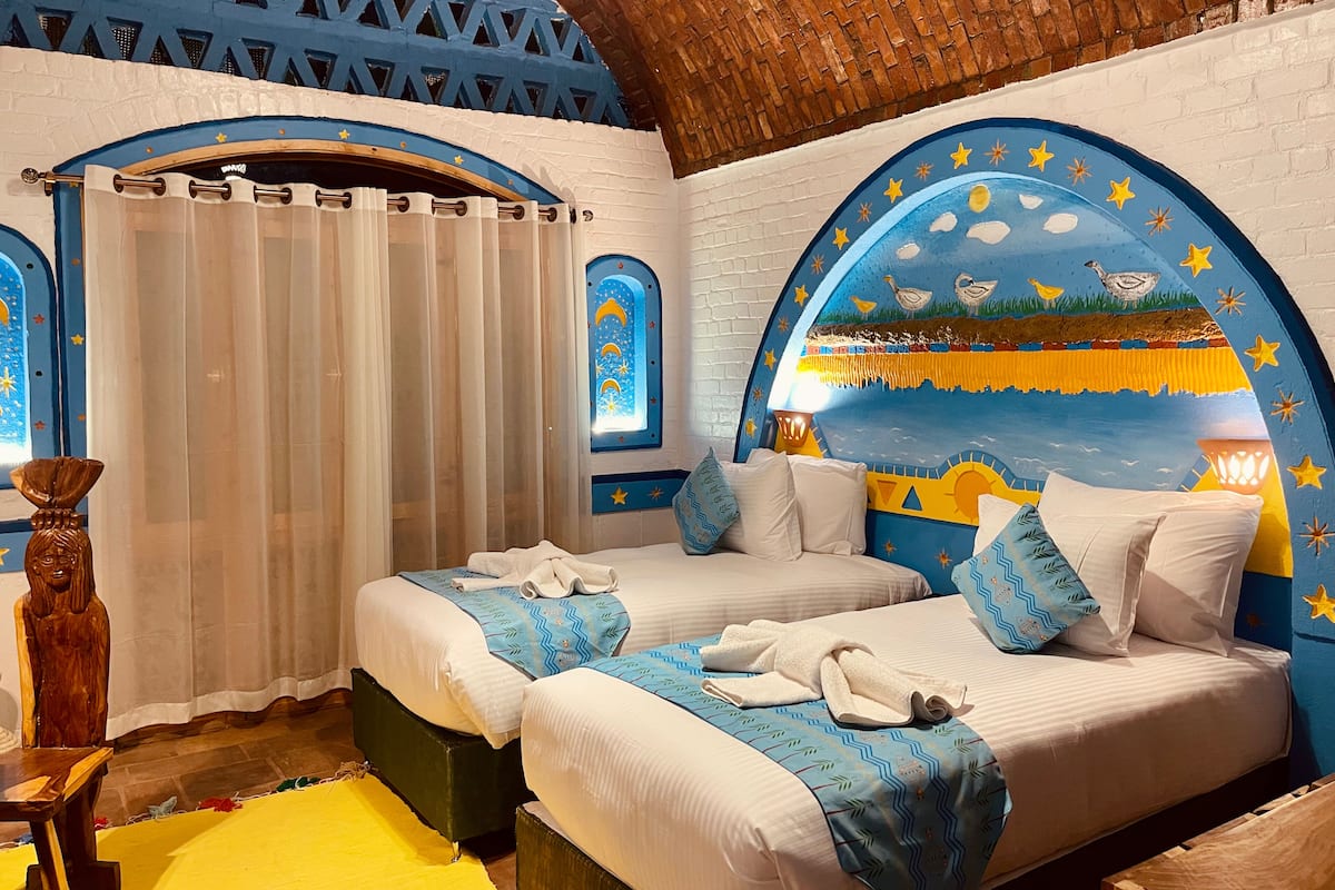 A room with two beds, a wooden chair, a yellow rug, and a mural on the wall.