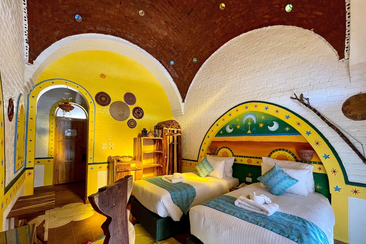 A room with two beds, a wooden bench, and a decorative archway.