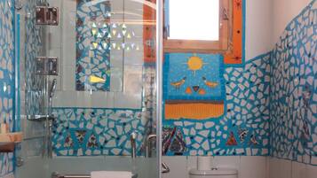 Un baño con cabina de ducha de vidrio, inodoro blanco y diseño de mosaicos en las paredes.