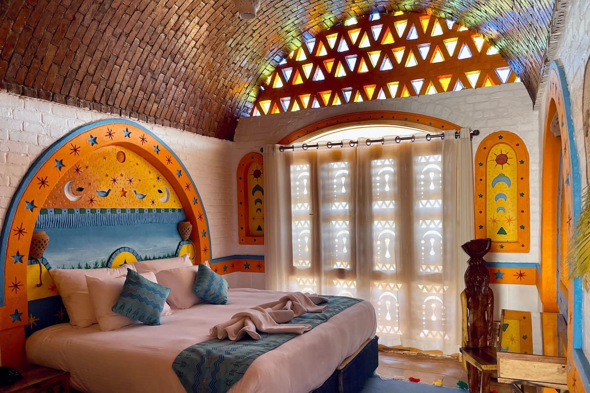 A room with a bed, a nightstand, a wooden chair, and a window with a view of the sky.