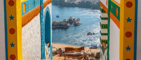 A colorful arched window with a view of a beach and rocky outcrops.