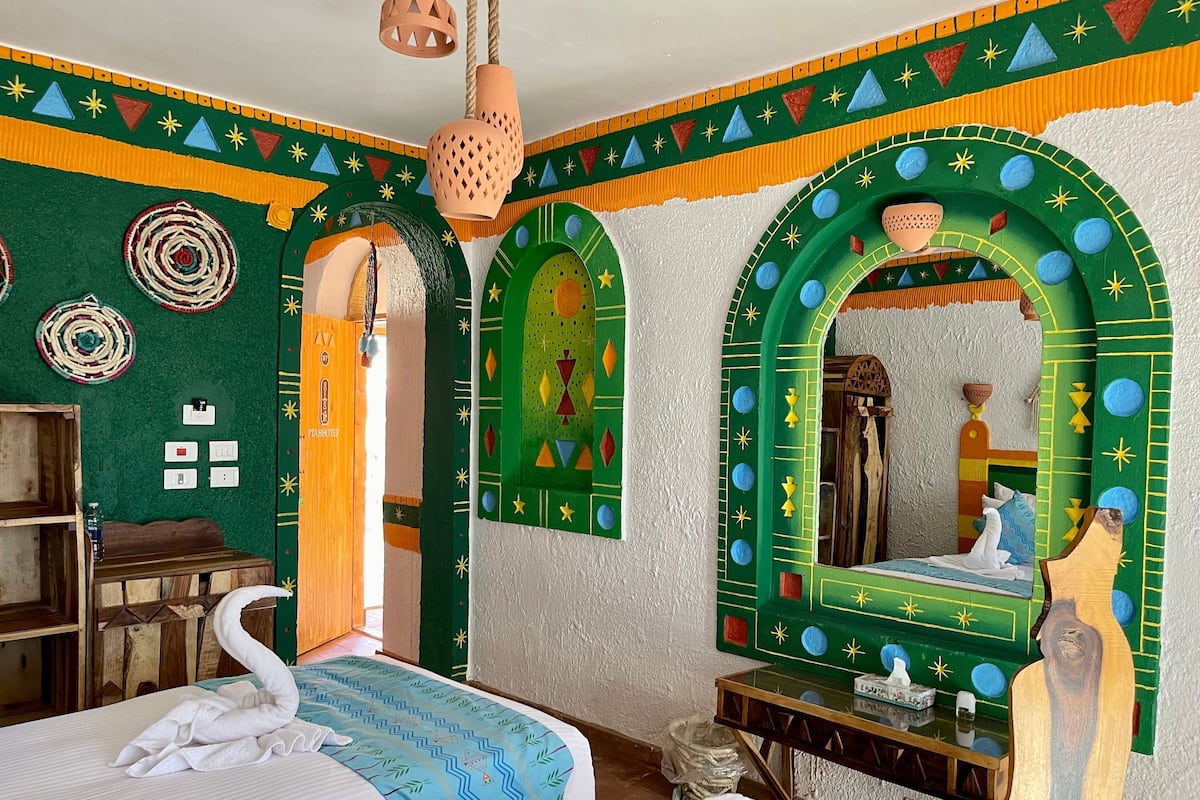 A room with a bed, a wooden cabinet, a mirror, and a wall with decorative patterns.