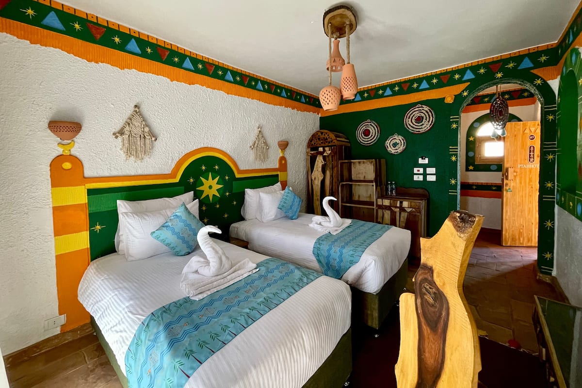A room with two beds, a wooden headboard, a wall with decorative patterns, and a small wooden cabinet.