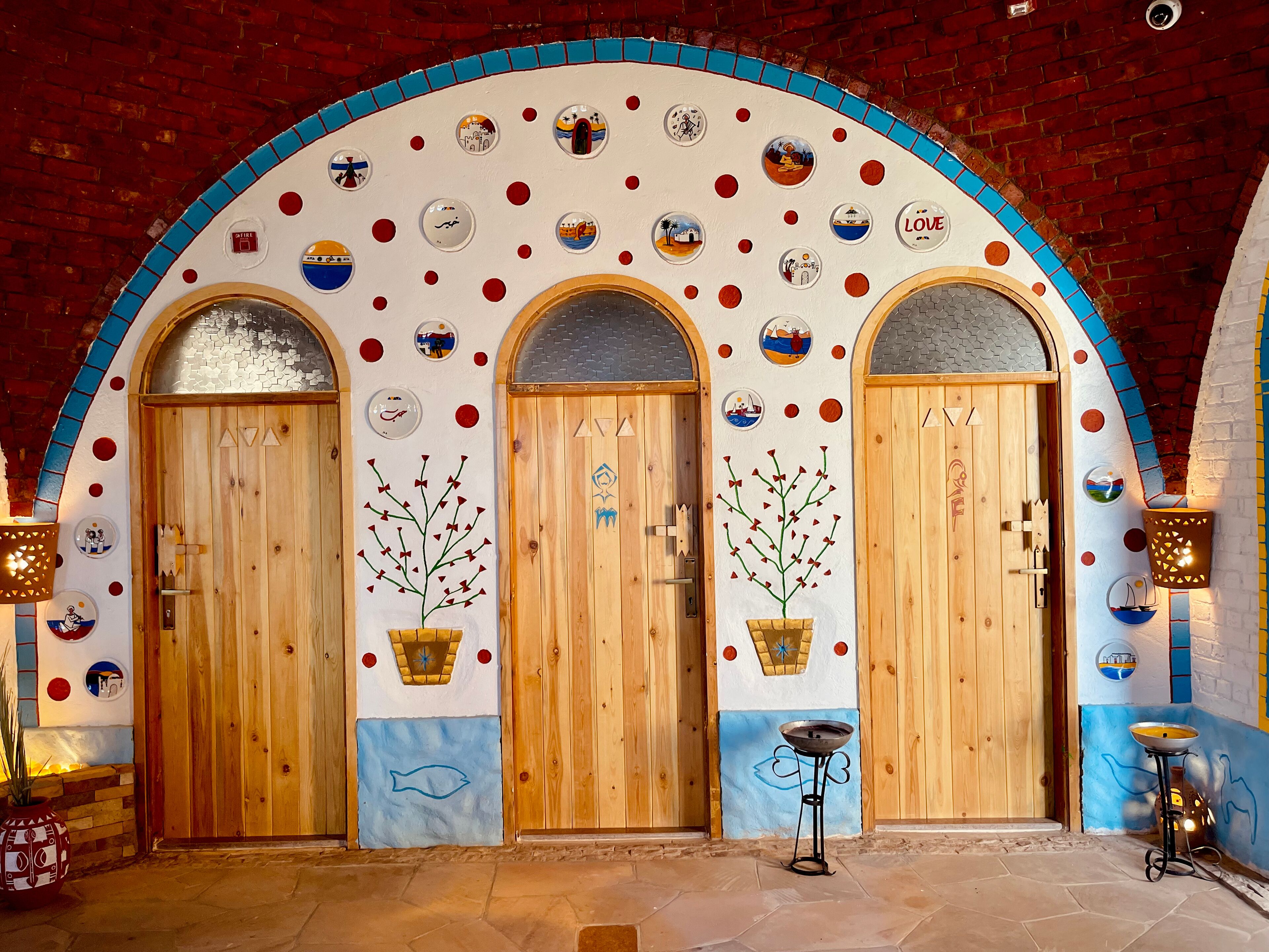 Entrada de hotel con tres puertas de madera, cada una decorada con ilustraciones de pared coloridas y un esquema de colores azul y blanco.