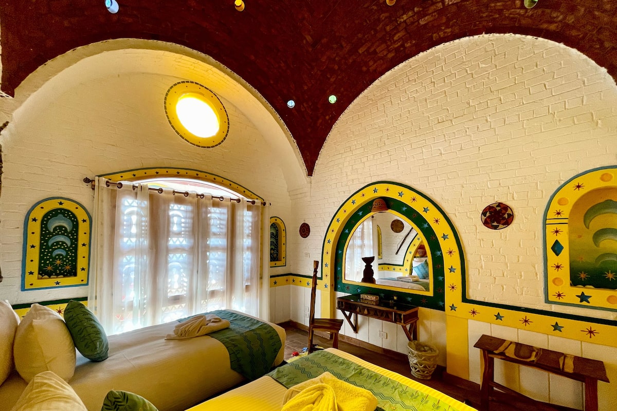 A room with two beds, a mirror, and a window with curtains.