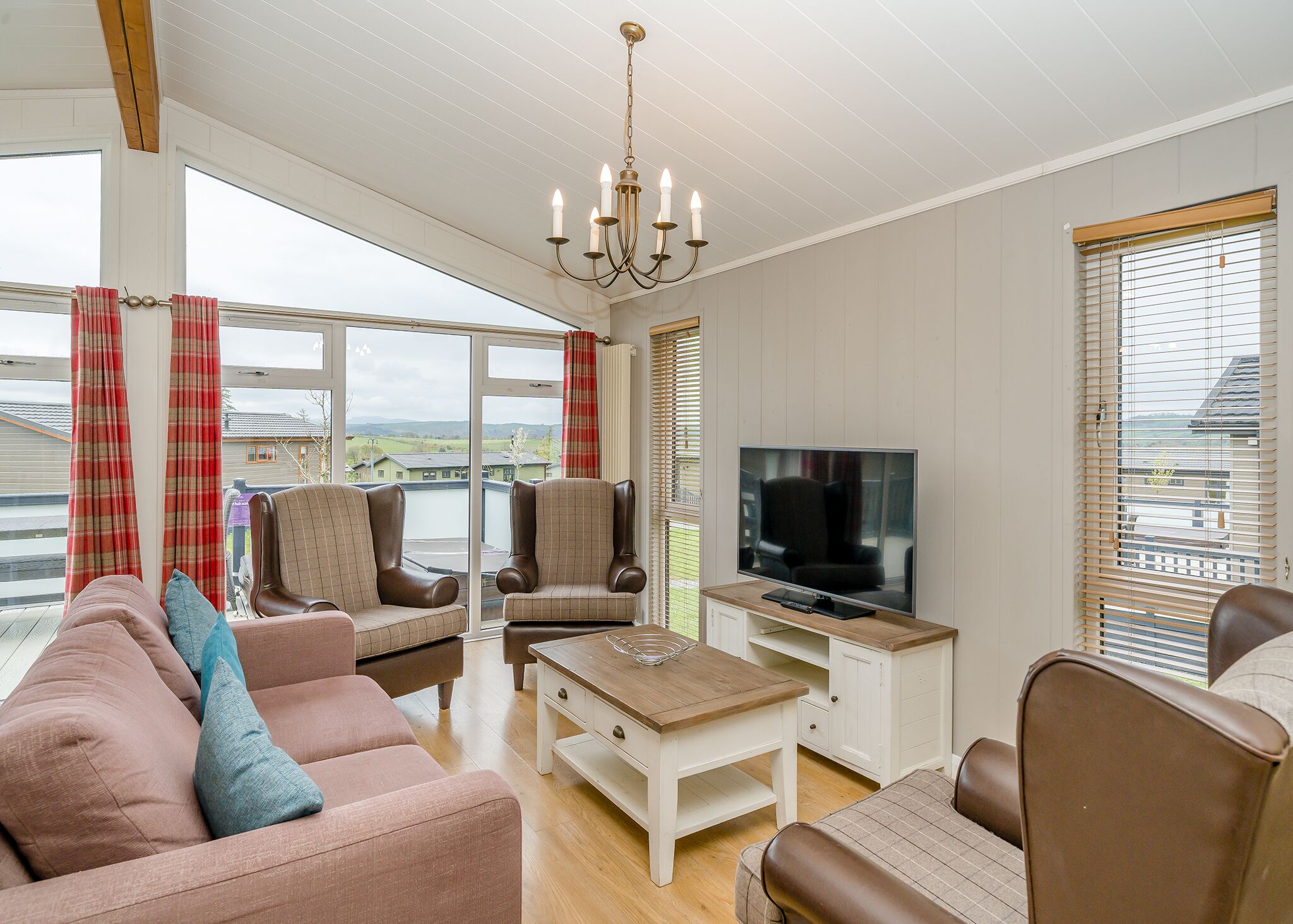 A living room with a sofa, chairs, a coffee table, a TV, and large windows with curtains.