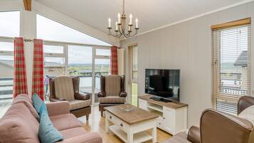 A living room with a sofa, chairs, a coffee table, a TV, and large windows with curtains.
